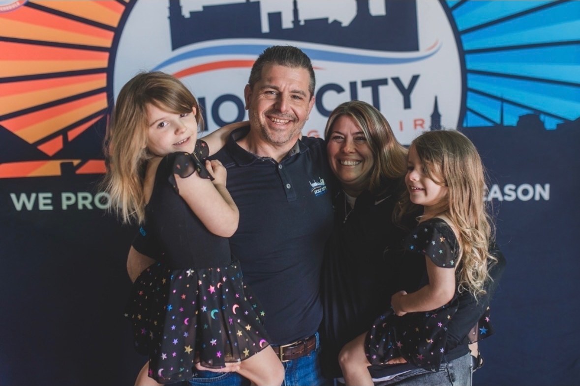 Tom and Jennifer Harvey with their daughters in front of the Holy City Heating & Air backdrop